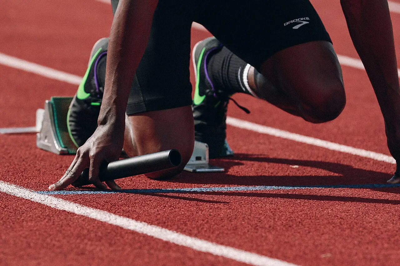 A sprinter crouched at the start line holding a relay baton