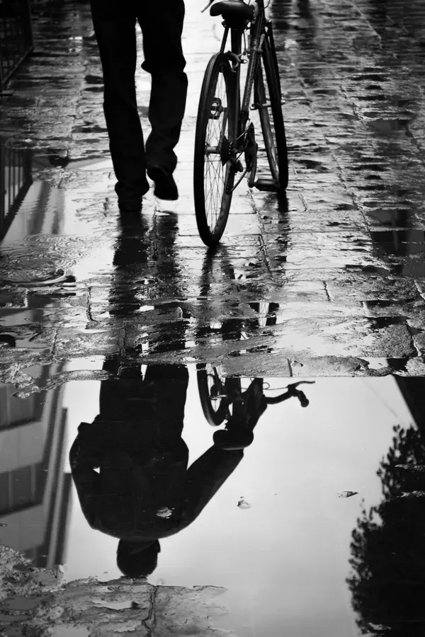 A person's reflection in a rain puddle on the pavement